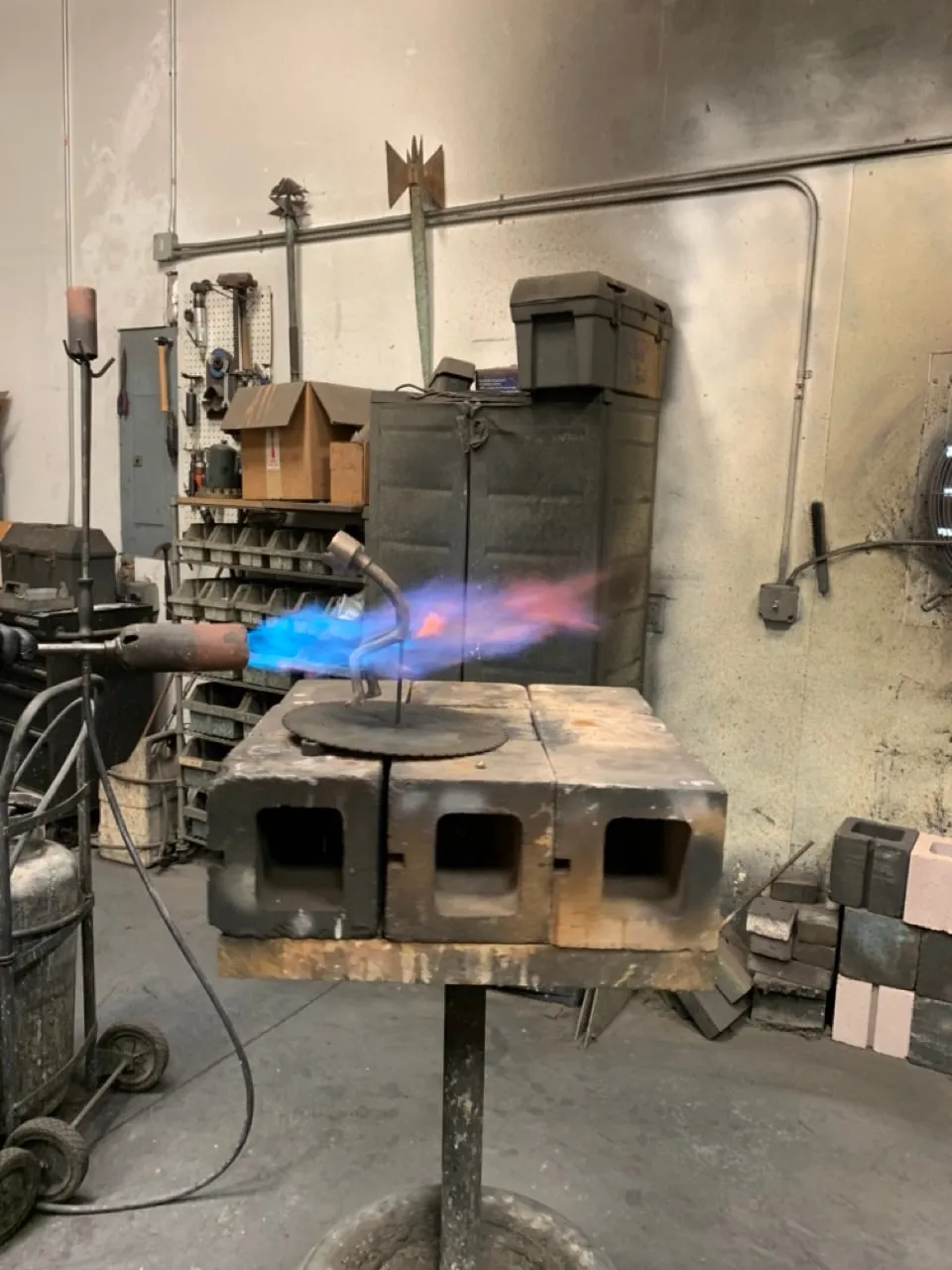 A blue torch flame playing over a small bronze on firebricks