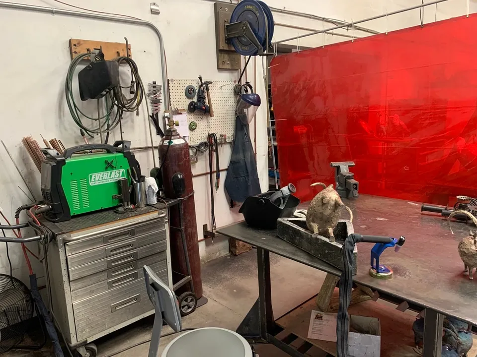 A welding bay with red screens, a welder and hoses on the wall
