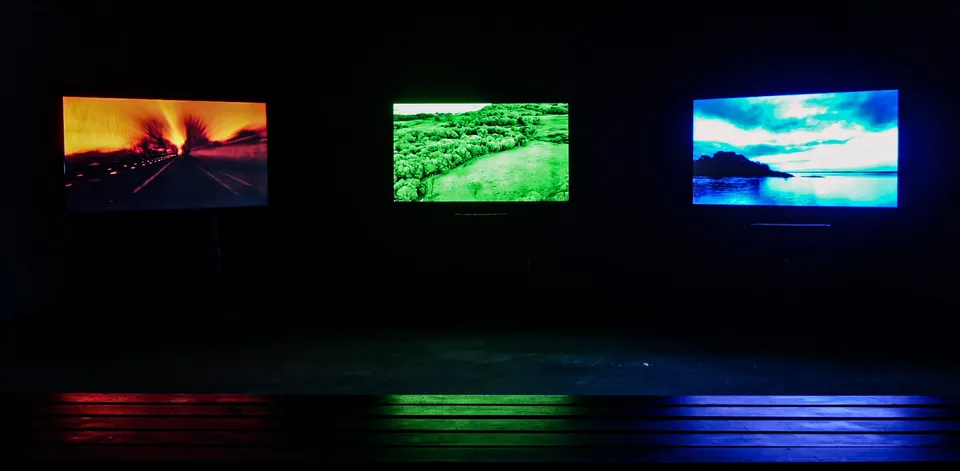 The three screens showing a burning road, green fields and a blue coastline
